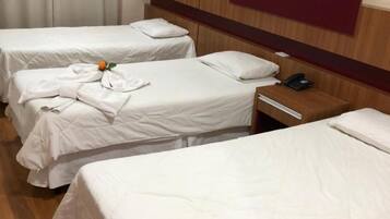 Habitación de hotel con tres camas individuales, cabeceros de madera y una mesita de noche con teléfono.