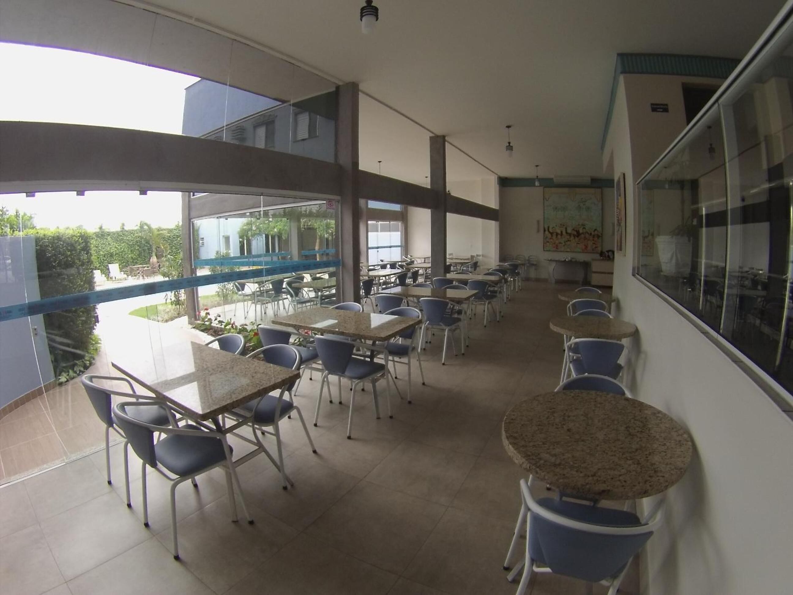A spacious outdoor dining area with multiple tables and chairs, large windows offering views of the surrounding area, and a modern architectural design.