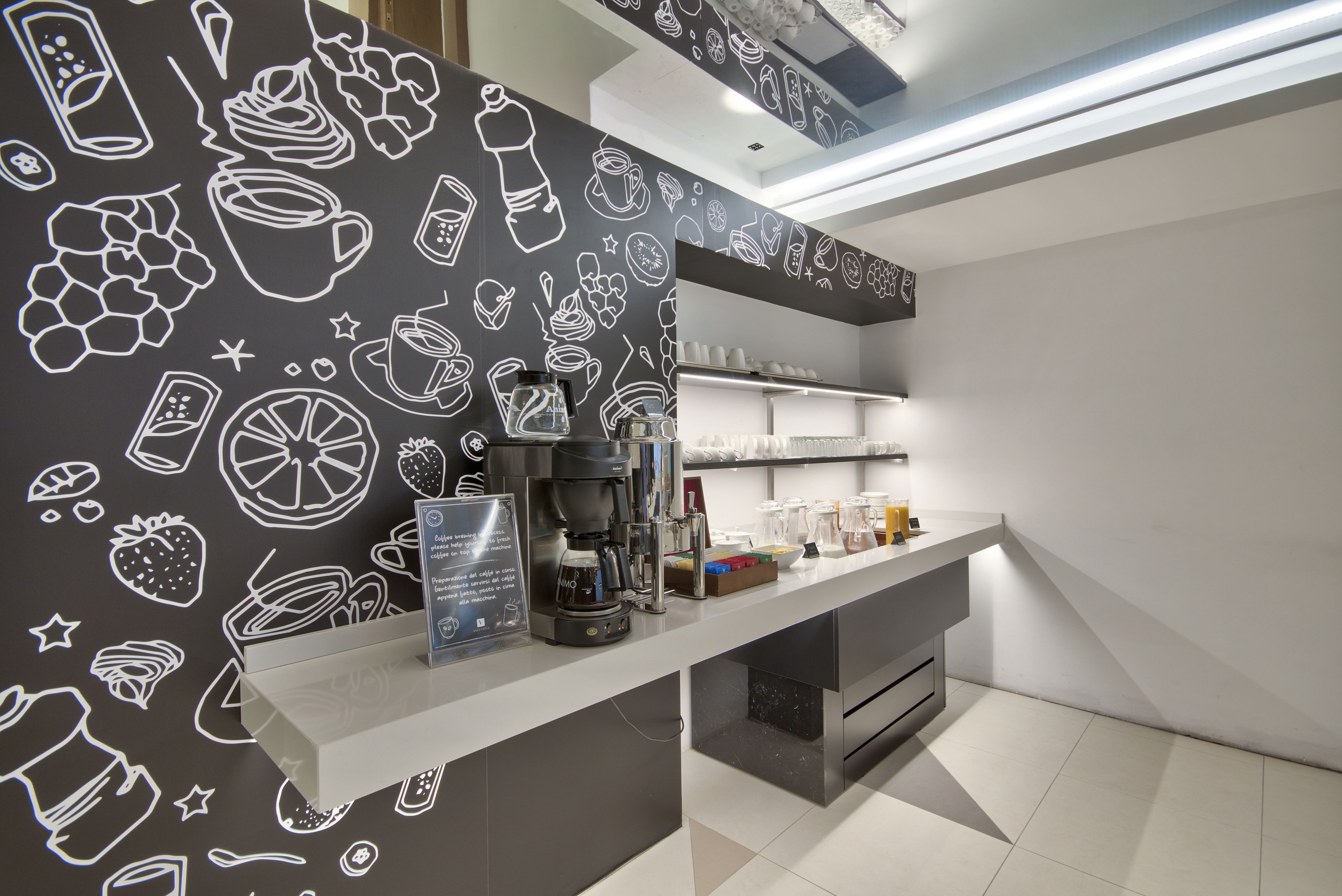 Eine moderne Küche mit einer Kaffeestation, weißen Arbeitsplatten und einer Wand mit Illustrationen von Lebensmitteln und Getränken.