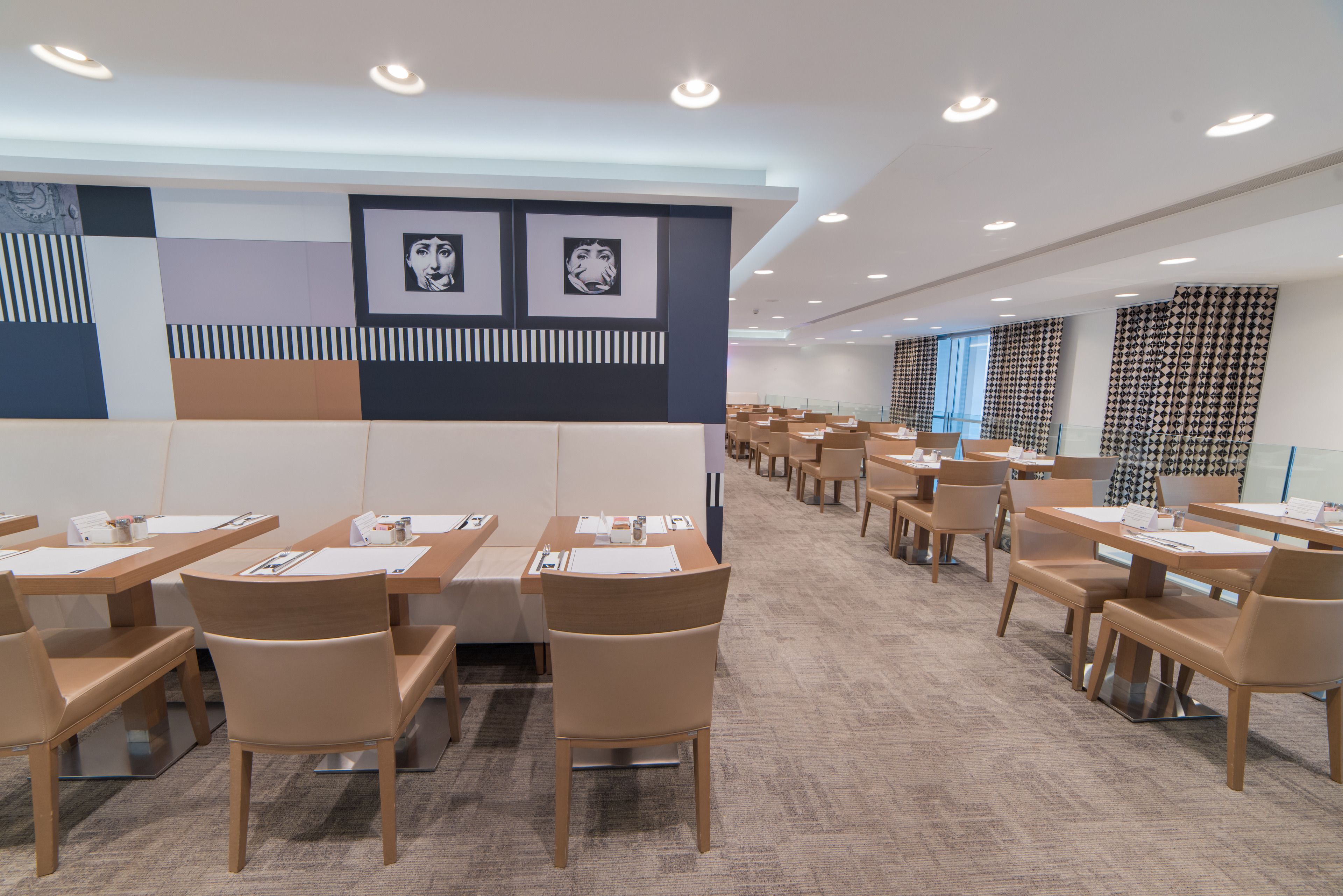A modern dining area with multiple tables and chairs, a patterned wall, and ceiling lights.