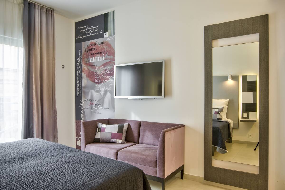 Una camera d'albergo con un letto, un divano, una televisione, uno specchio e un quadro appeso al muro.