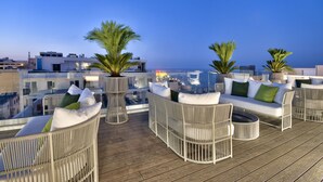 A rooftop terrace with wicker furniture, palm trees, and a view of the cityscape at dusk. - Hotel Valentina (St. Julian's)