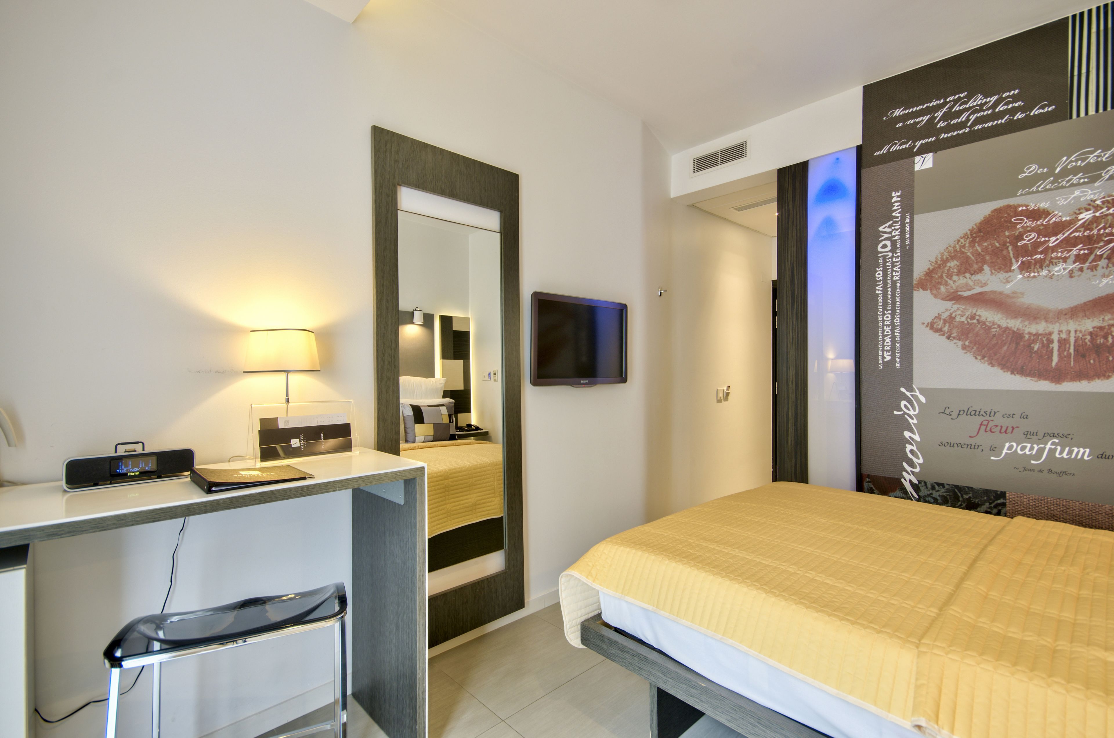 Ett hotellrum med en säng, ett skrivbord med en stol, en tv och en stor affisch på väggen.