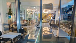 A modern hotel lobby with a glass partition, seating area with tables and chairs, a staircase, and a bar area. - Hotel Valentina (St. Julian's)