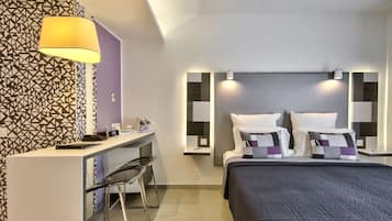 Ett modernt hotellrum med ett skrivbord, stolar, en säng med ett mörkt täcke och tapet med geometriskt mönster.