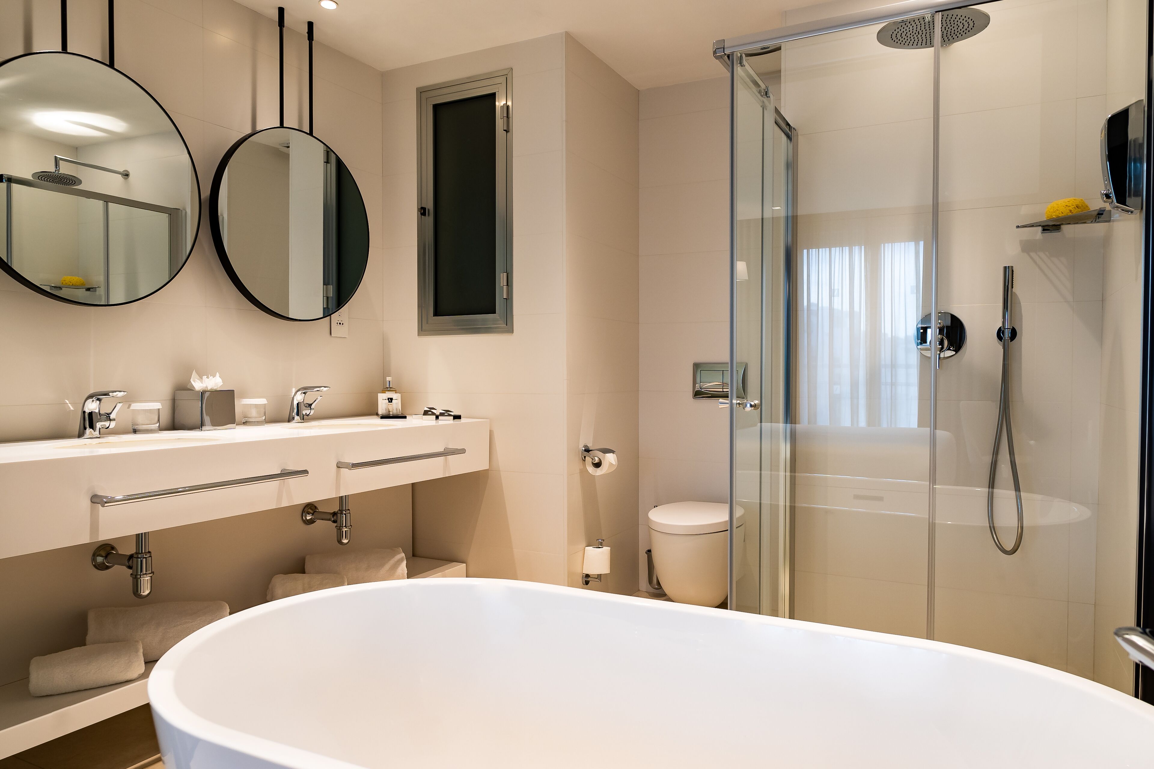 A modern bathroom with a freestanding bathtub, a glass-enclosed shower, and two wall-mounted mirrors.