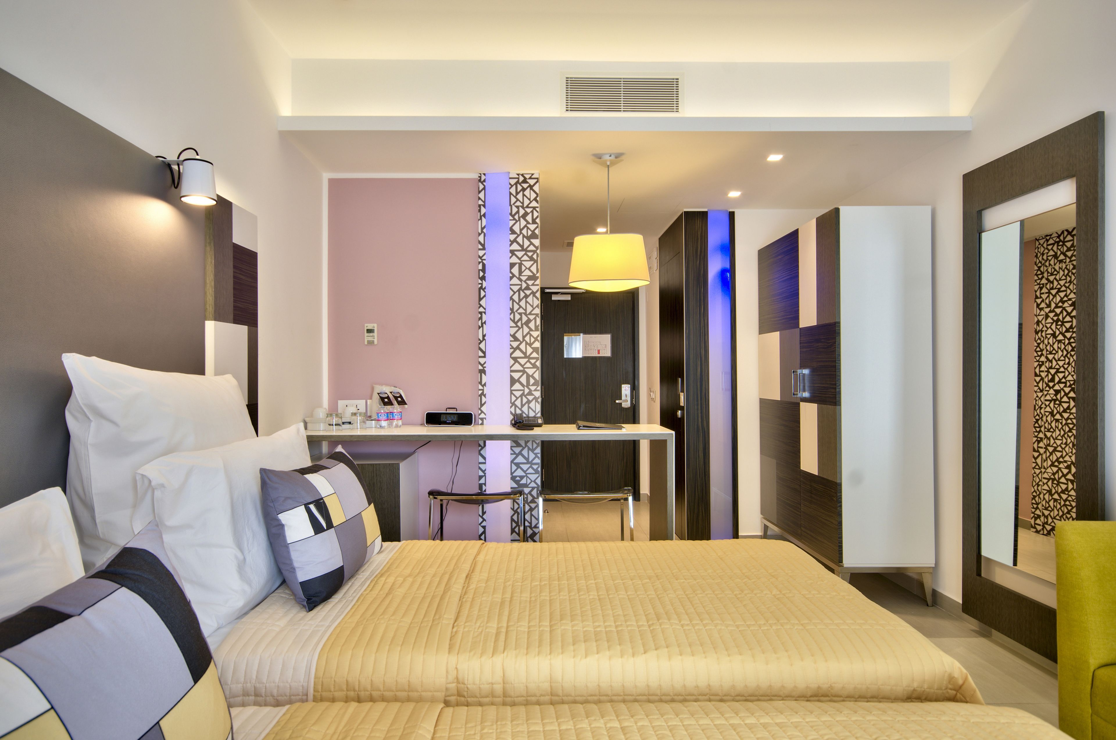 A modern hotel room with a large bed, bedside table, and a desk with a chair.
