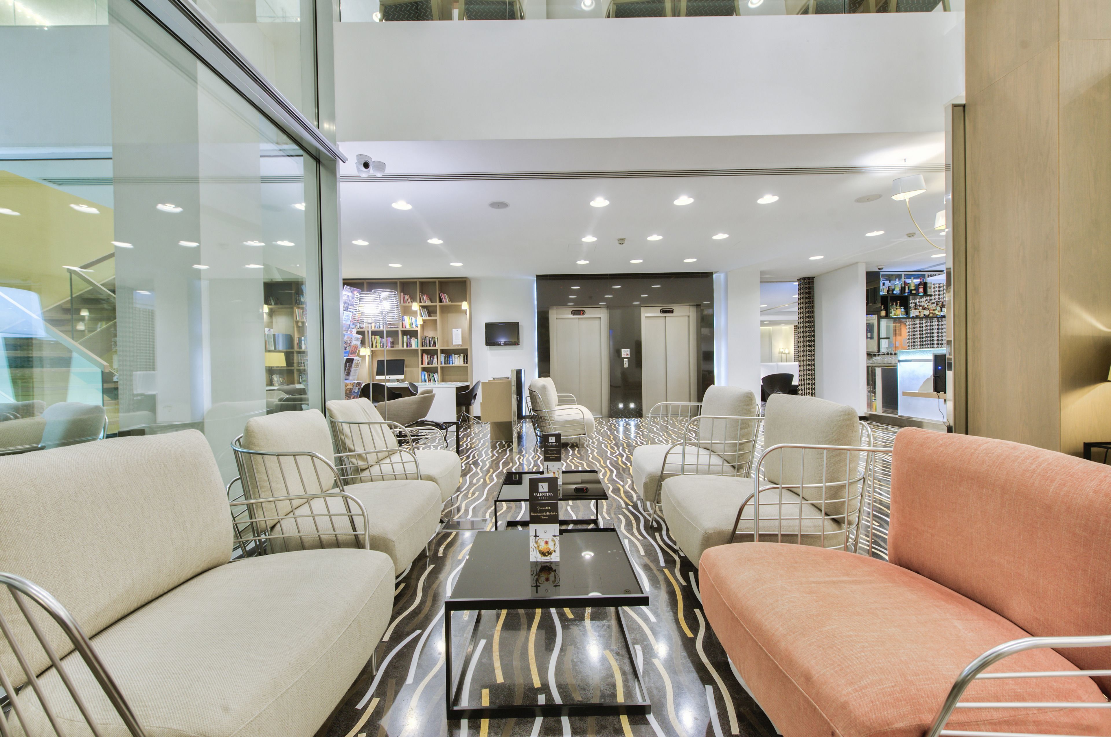 A modern lobby with seating areas, a reception desk, and a staircase leading to an upper level.