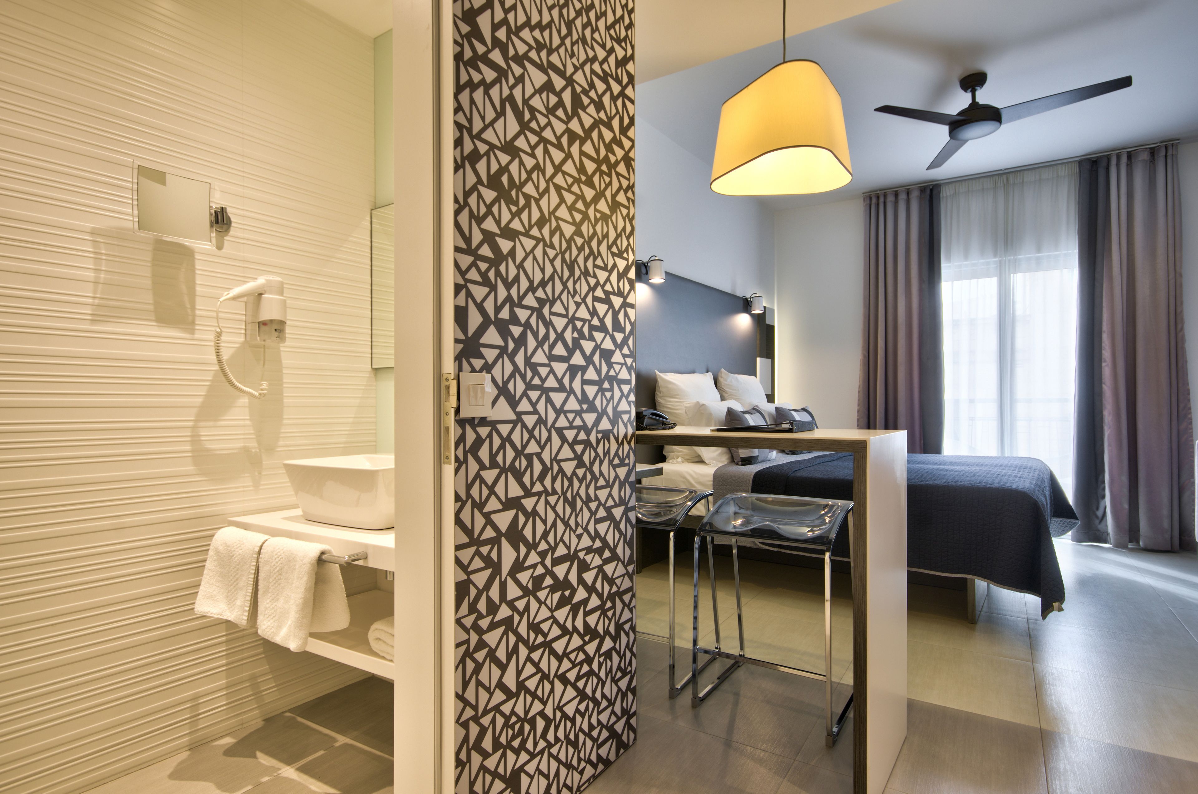 Une chambre d’hôtel moderne équipée d’une douche, d’un lit, d’un bureau et d’un ventilateur de plafond.