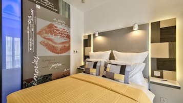 A modern hotel room with a large bed, a nightstand, a wall-mounted lamp, and a decorative wall with text and a lipstick print.