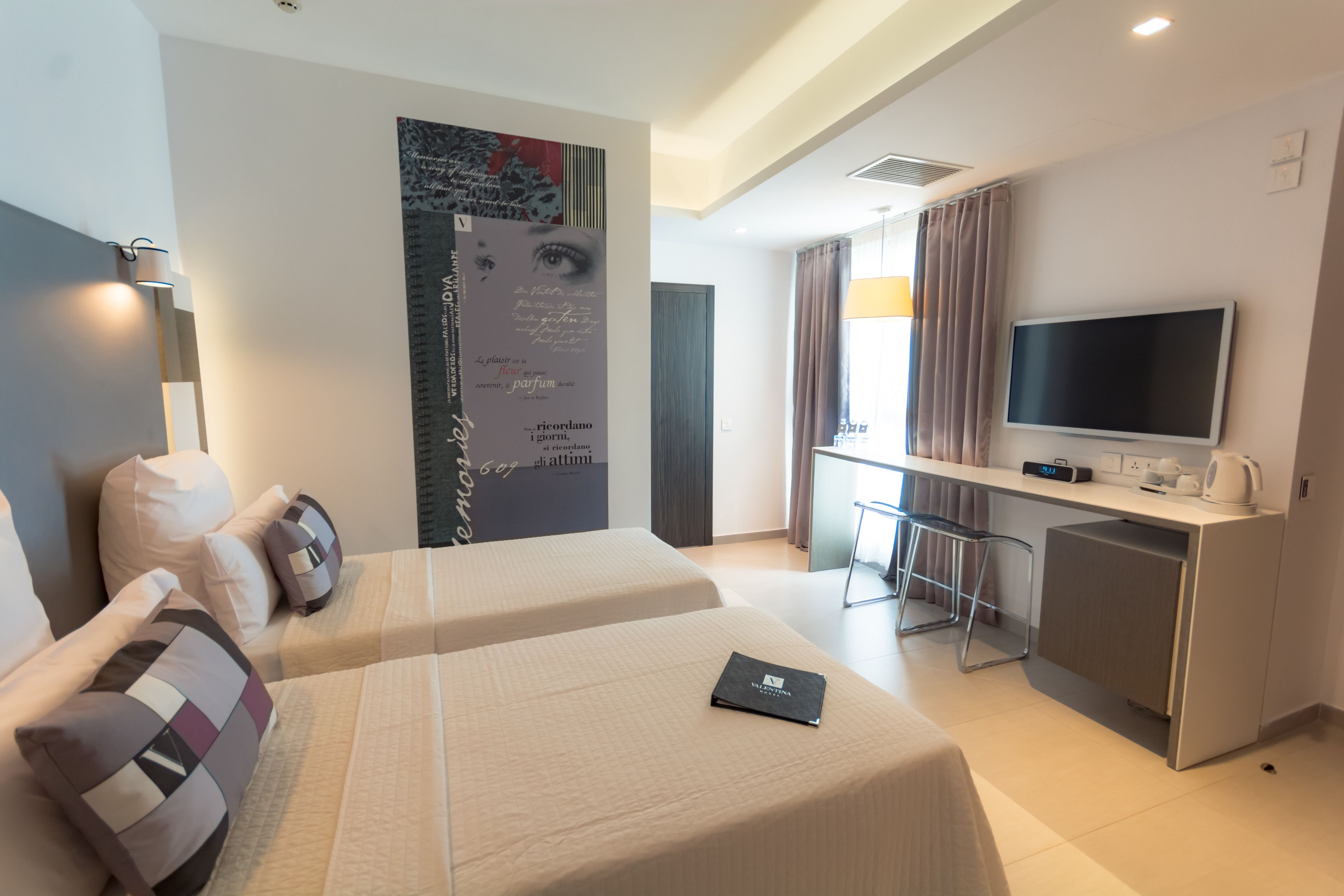 A hotel room with two beds, a desk with a TV, a coffee maker, and a large poster on the wall.