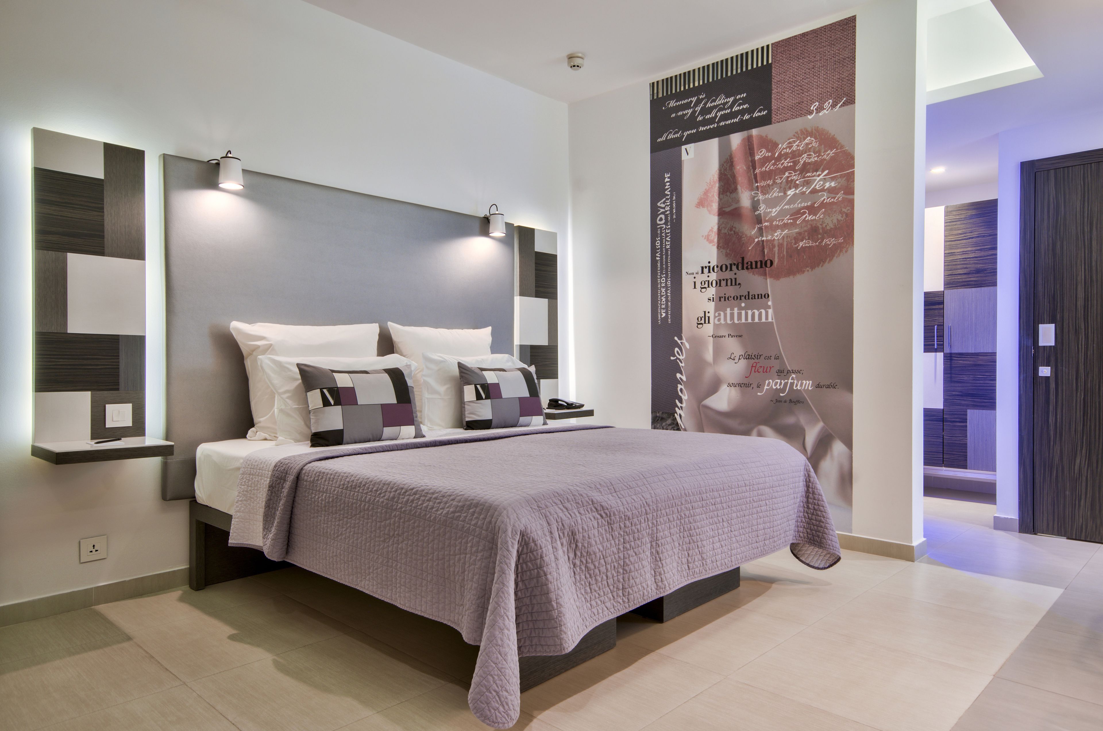 A modern bedroom with a large bed, bedside tables, and a wall-mounted light fixture.