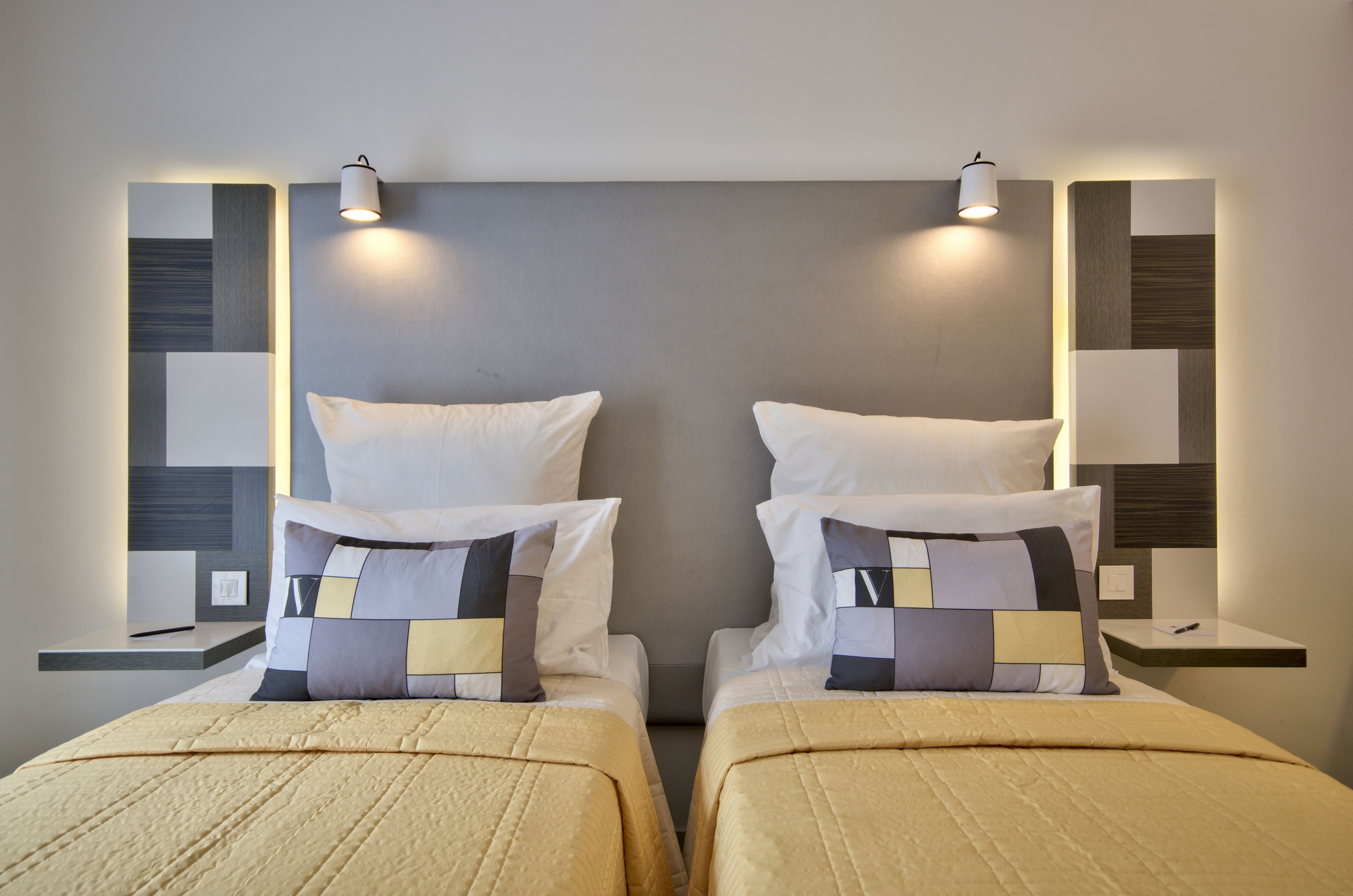 A hotel room with two beds, each with a quilted bedspread and pillows, and bedside tables with lamps.
