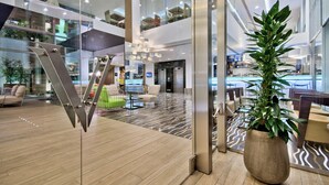 A modern hotel lobby with a central staircase, seating areas, and a large potted plant. - Hotel Valentina (St. Julian's)
