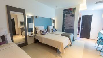 A modern hotel room with two beds, a large mirror, a wall-mounted TV, and a bathroom visible through an open door.