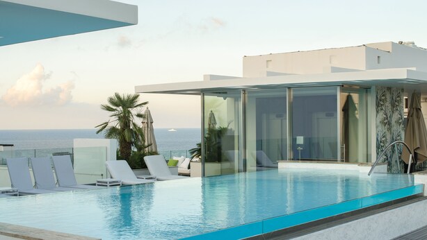 A modern infinity pool with clear blue water, surrounded by white lounge chairs and a glass-enclosed cabana. - Hotel Valentina (St. Julian's)