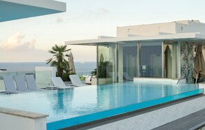 A modern infinity pool with clear blue water, surrounded by white lounge chairs and a glass-enclosed cabana. - Hotel Valentina (St. Julian's)
