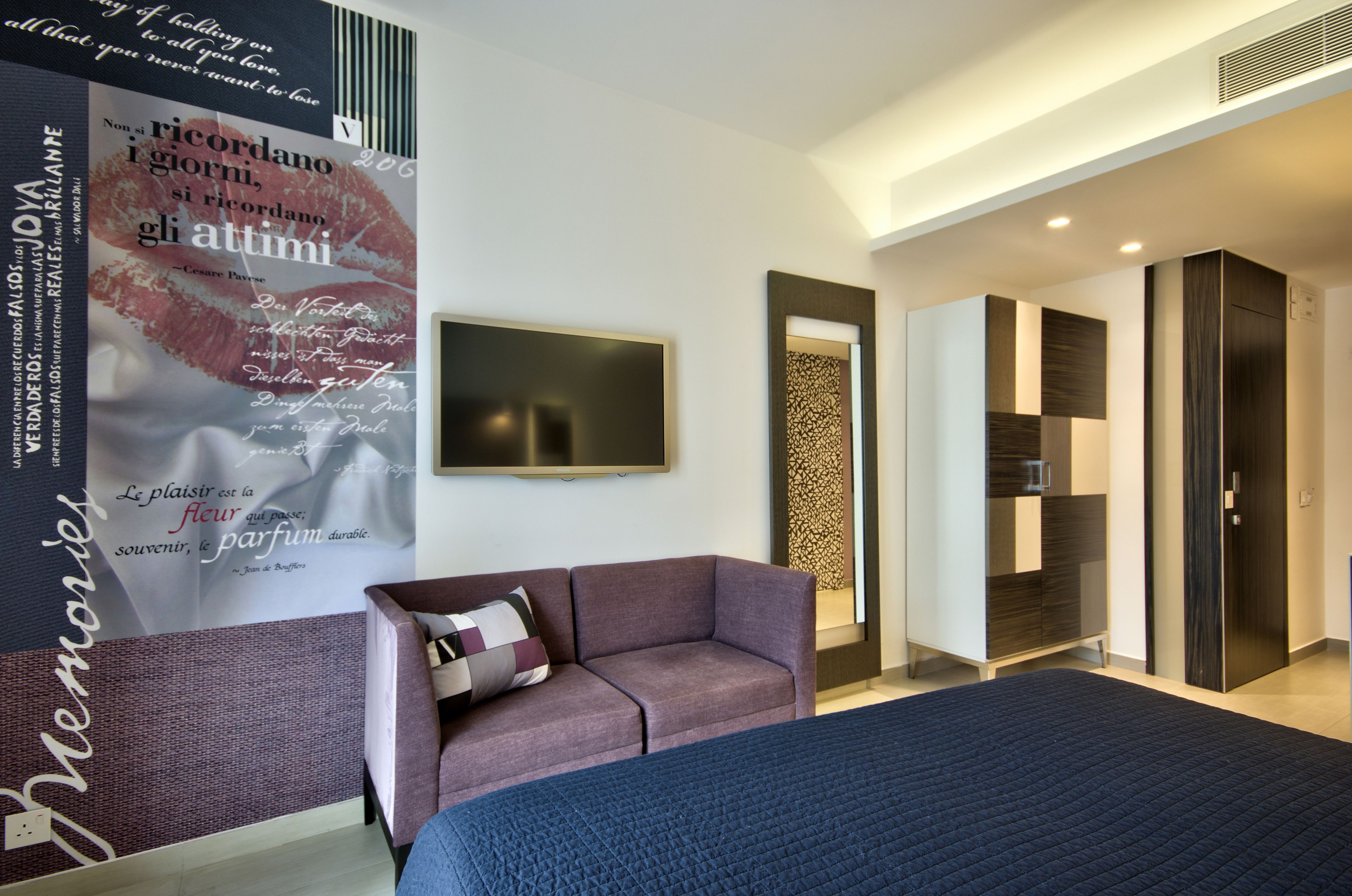 A modern hotel room with a large bed, a sofa, a flat-screen TV, and a poster on the wall.