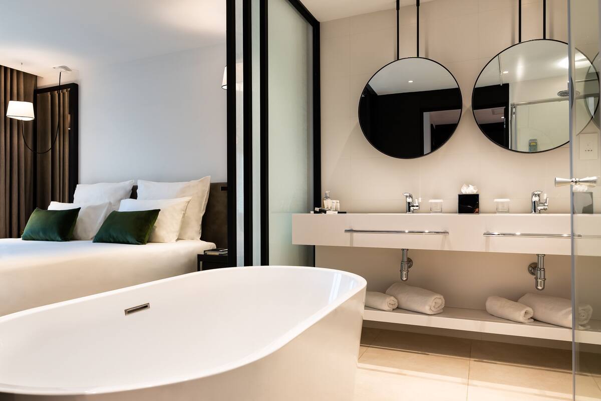 Una camera d'hotel moderna con un letto grande, una vasca freestanding e un doppio lavabo con specchi.