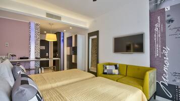 Une chambre d’hôtel avec un lit, un fauteuil jaune, un bureau avec une lampe et un téléviseur fixé au mur.