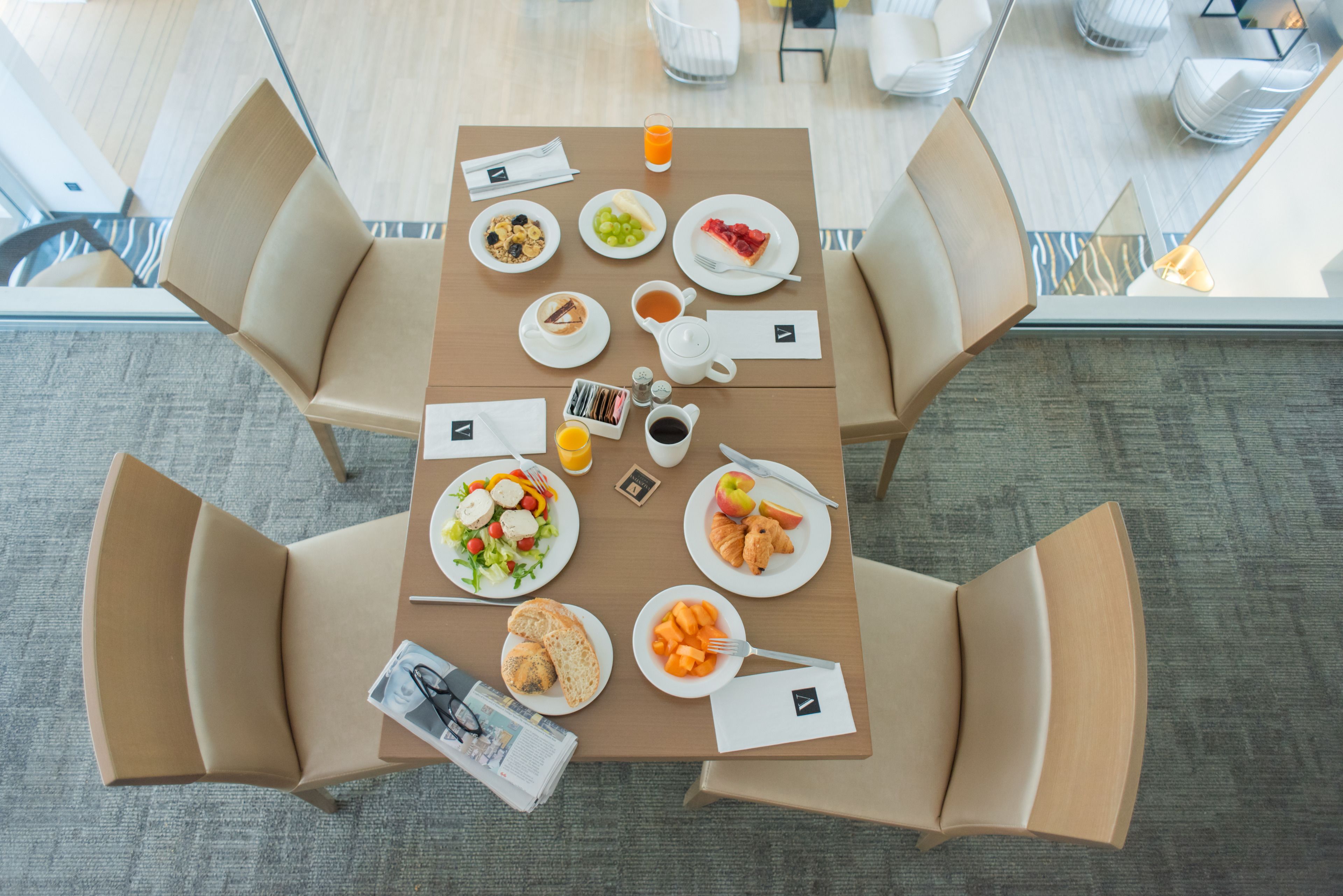 Ein Frühstückstisch reichhaltig gedeckt mit Früchten, Gebäck und Getränken in einem modernen Hotelzimmer.
