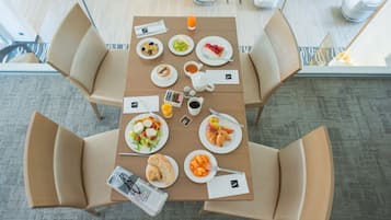 Ein Frühstückstisch reichhaltig gedeckt mit Früchten, Gebäck und Getränken in einem modernen Hotelzimmer.