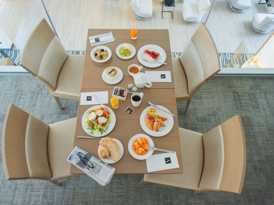 Ein Frühstückstisch reichhaltig gedeckt mit Früchten, Gebäck und Getränken in einem modernen Hotelzimmer.
