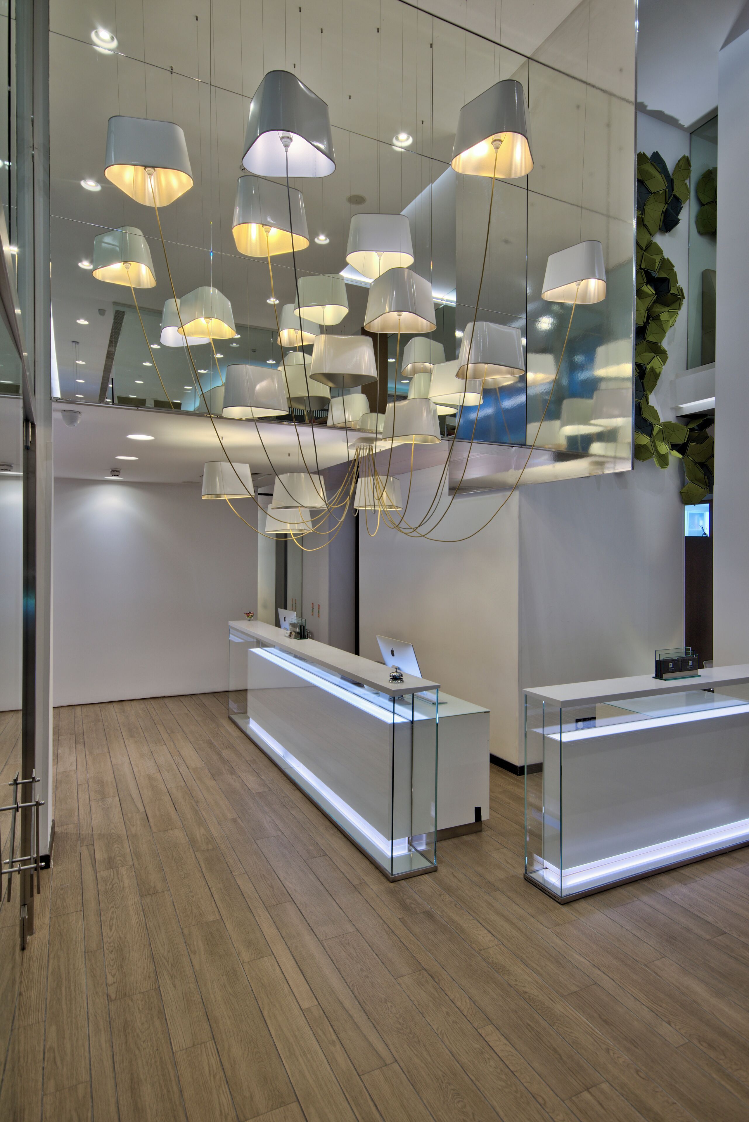 Un área de recepción moderna con suelo de madera, mostradores de recepción de vidrio e iluminación colgante.