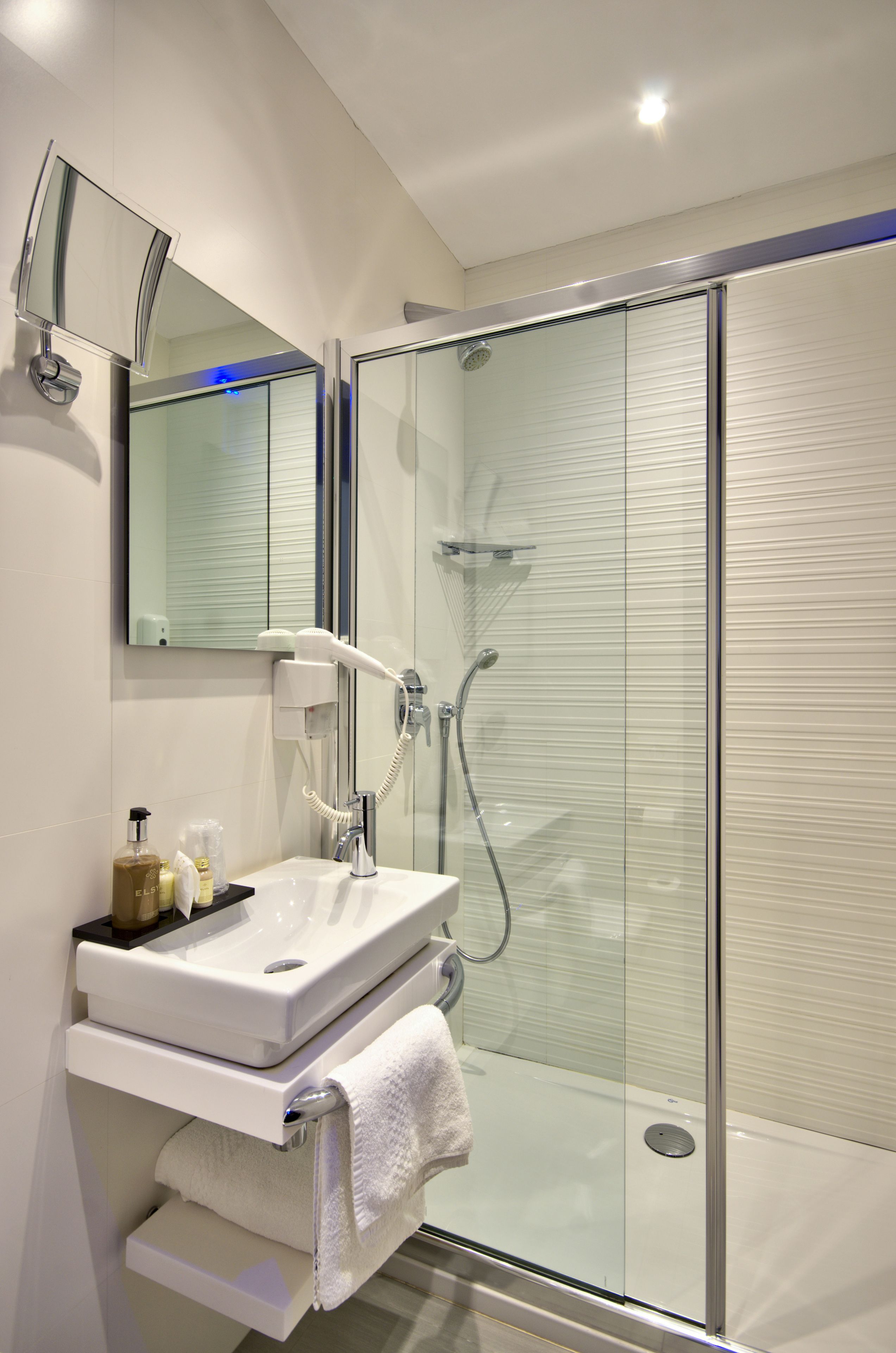 Un bany modern amb dutxa de vidre, un lavabo blanc i un mirall a sobre.