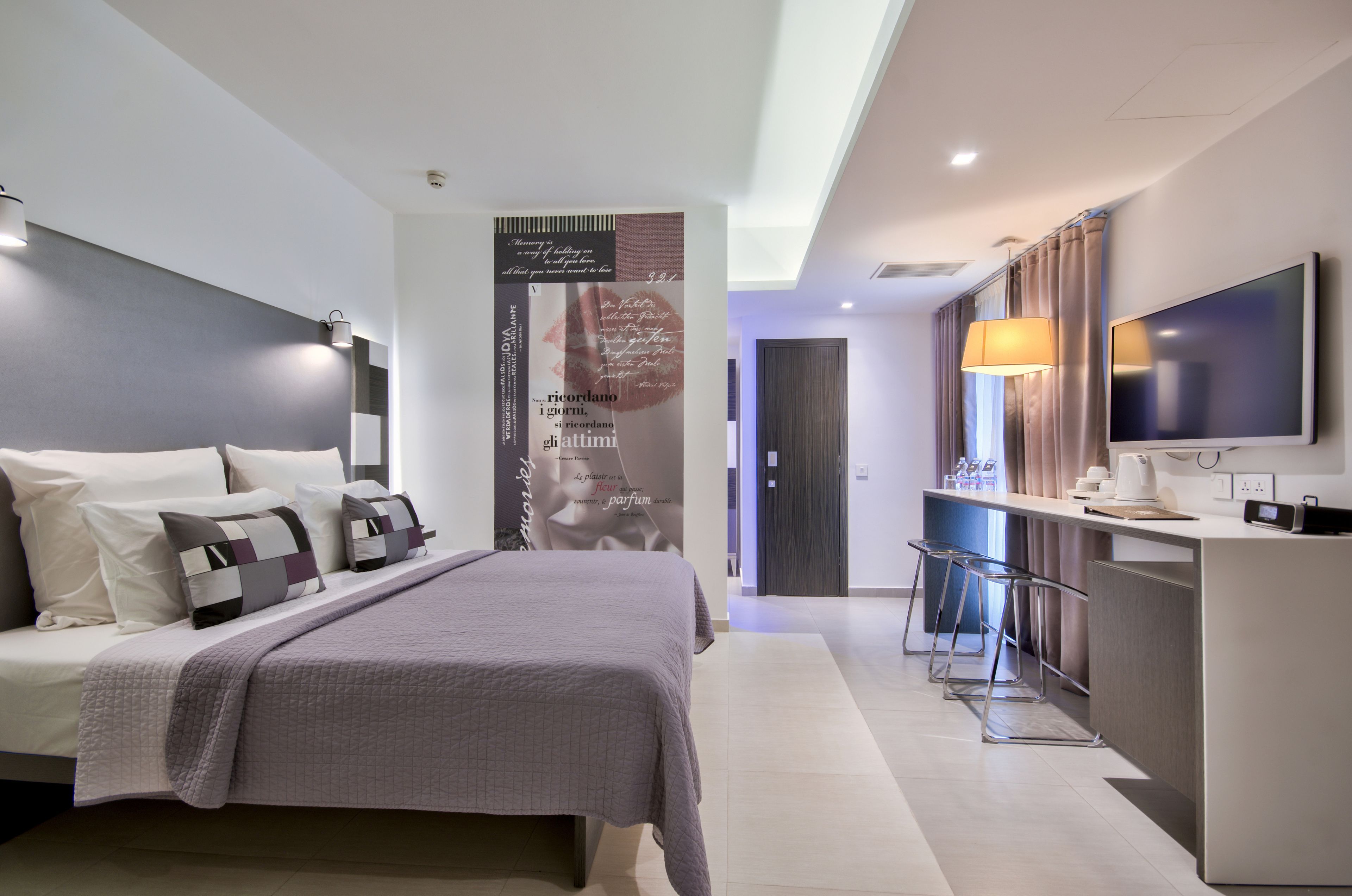 A modern hotel room with a bed, a TV, a desk, and a bar area.