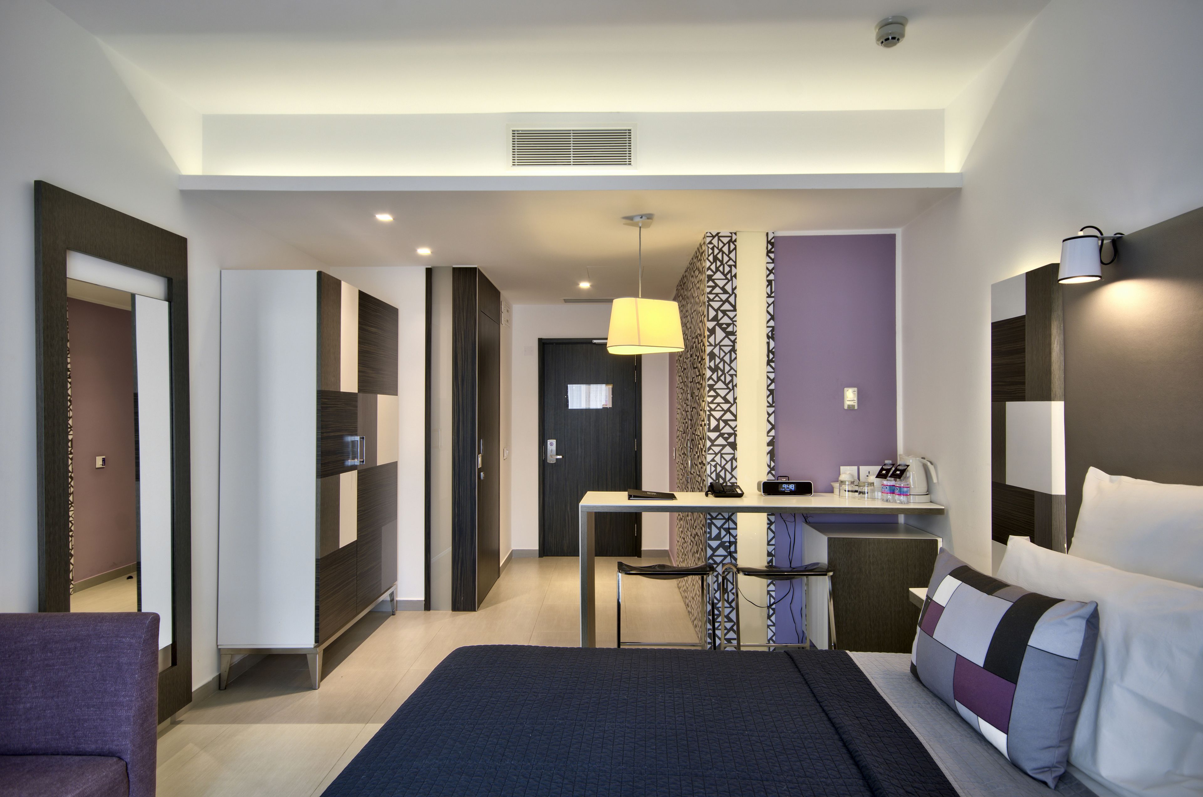 A modern hotel room with a bed, a desk, a chair, and a small table.