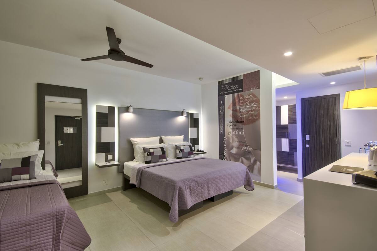 Camera d'albergo moderna con un letto, comodini, ventilatore a soffitto e bagno con specchio e portasciugamani.
