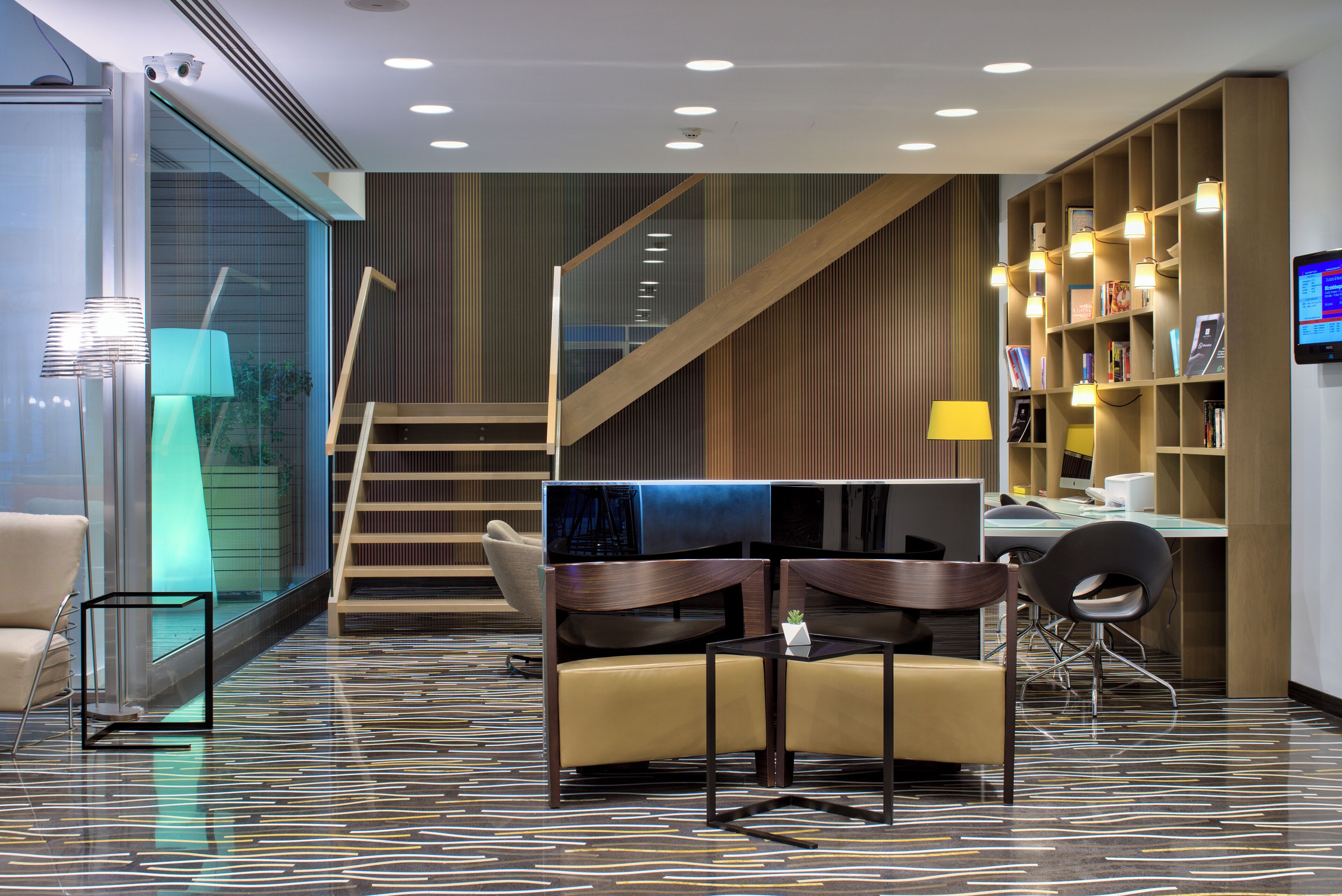 A modern hotel lobby with a staircase, seating area, and a bookshelf.