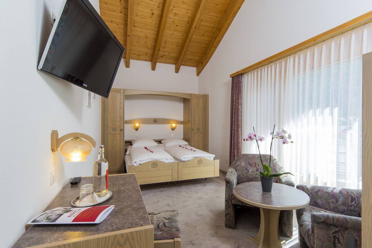 A hotel room with a bed, a desk with a lamp, a chair, a small table, and a TV mounted on the wall.