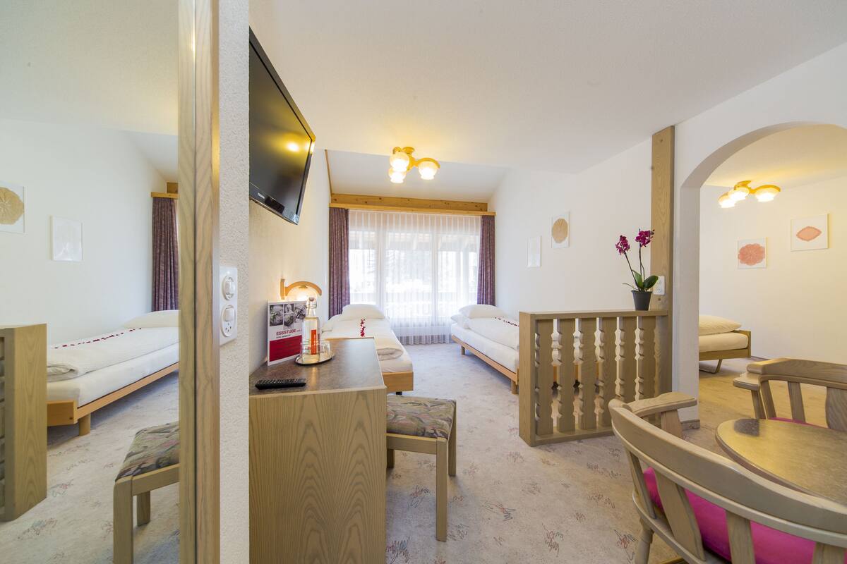 A hotel room with a bed, a desk, a chair, a dining table, and a TV mounted on the wall.