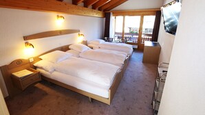A hotel room with a wooden ceiling, a large bed with white bedding, a nightstand, a TV mounted on the wall, and a balcony with a view.