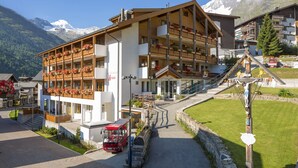 A multi-story hotel with balconies, a red bus, and a mountain backdrop.
