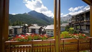 A mountain village with traditional buildings, a wooden fence with flowers, and a view of snow-capped mountains.