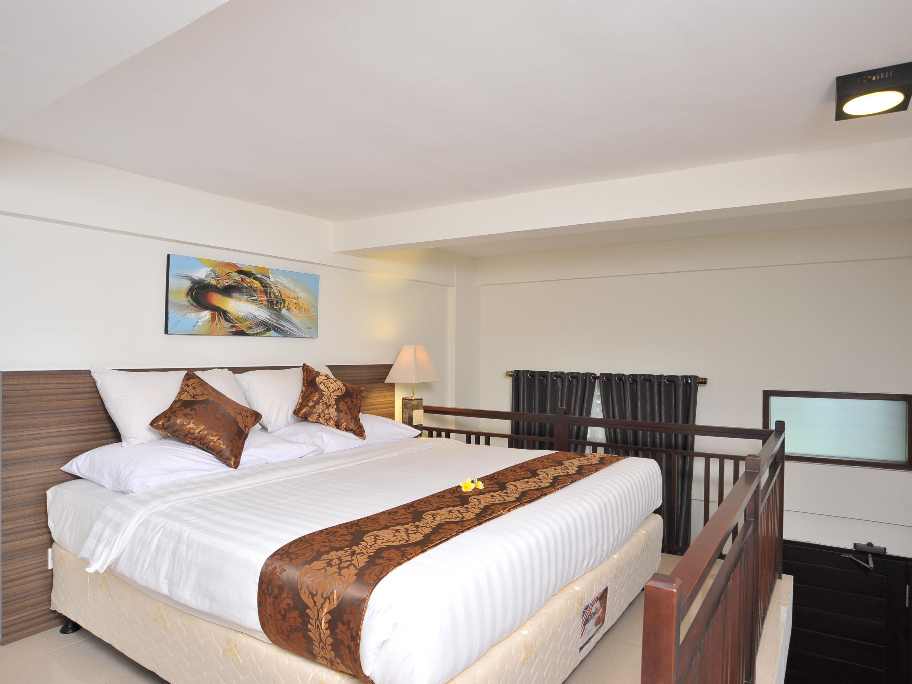A hotel room with a large bed, a painting on the wall, a lamp, and a view of the outside through a window.