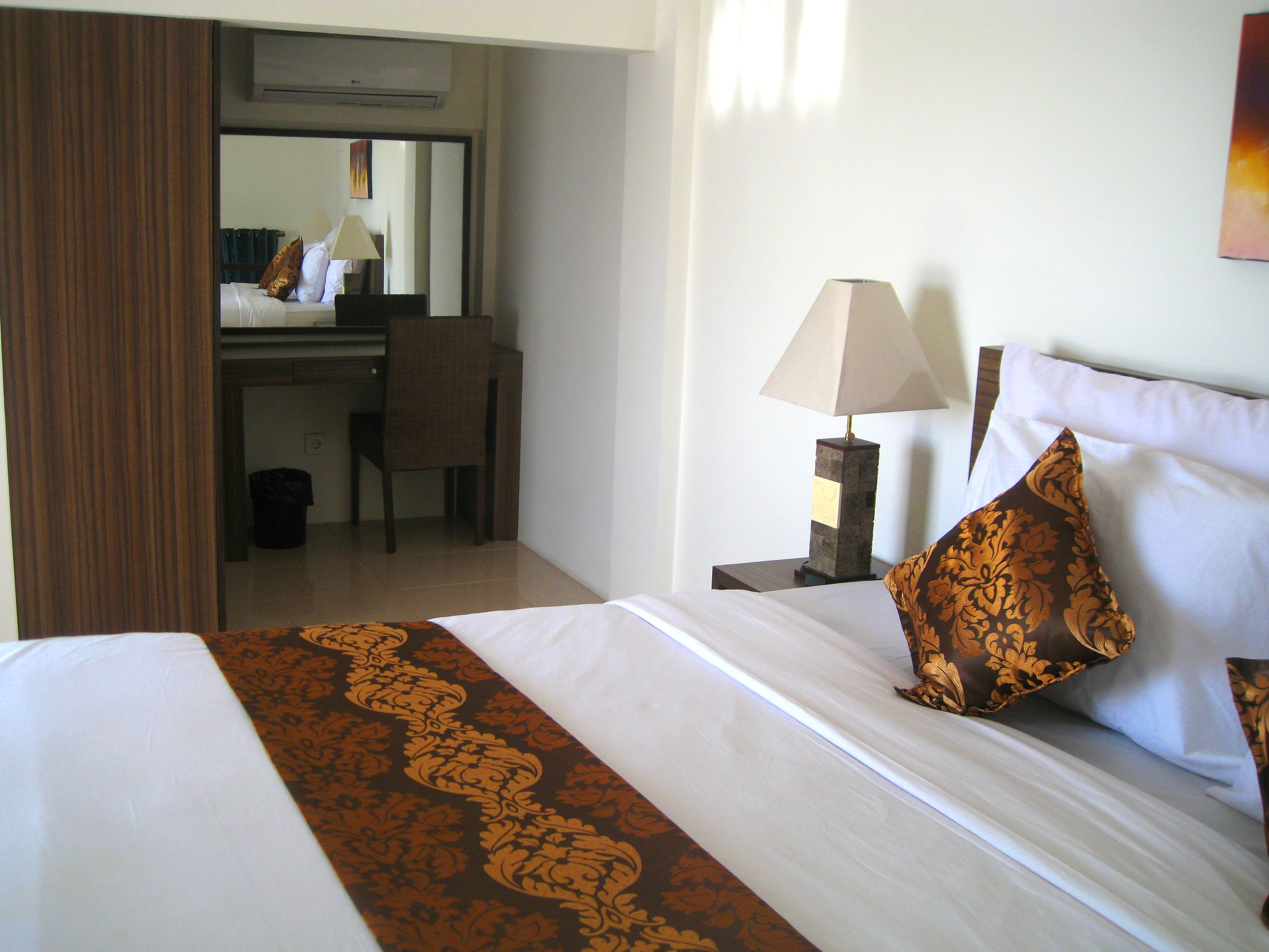 Una habitación de hotel con cama, escritorio, silla, lámpara y espejo.