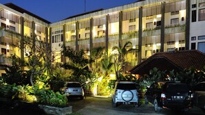 A multi-story hotel with a courtyard featuring parked cars and lush greenery. - Ganga Hotel & Apartments (Denpasar)