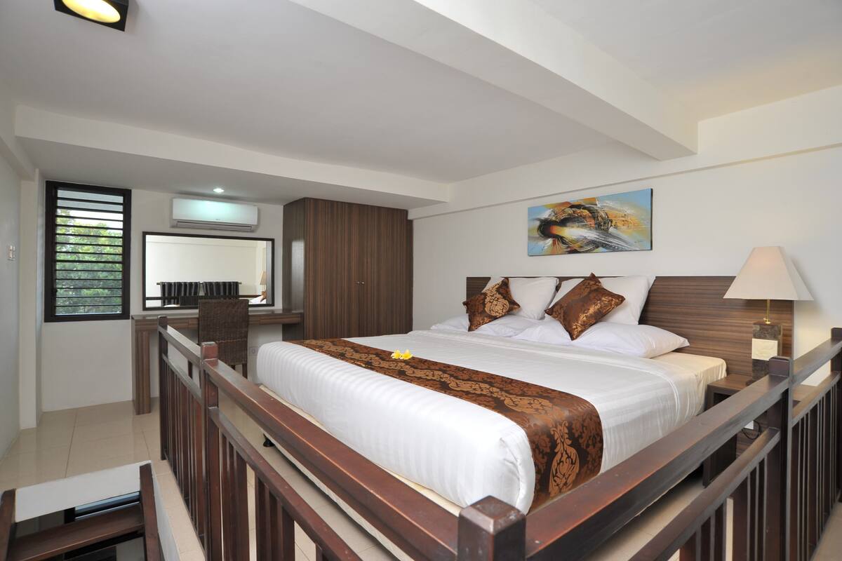 A neatly arranged hotel room with a large bed, a desk, and a window with blinds.
