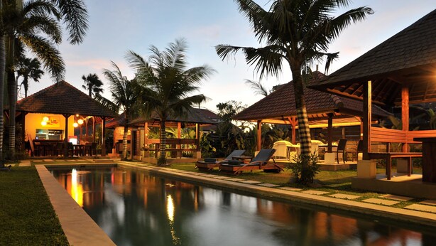 A poolside area with lounge chairs, a bar, and a covered seating area with palm trees. - Ganga Hotel & Apartments (Denpasar)