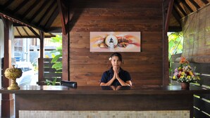 A reception desk with a wooden counter, a mosaic tile wall, and a framed artwork above it. - Ganga Hotel & Apartments (Denpasar)