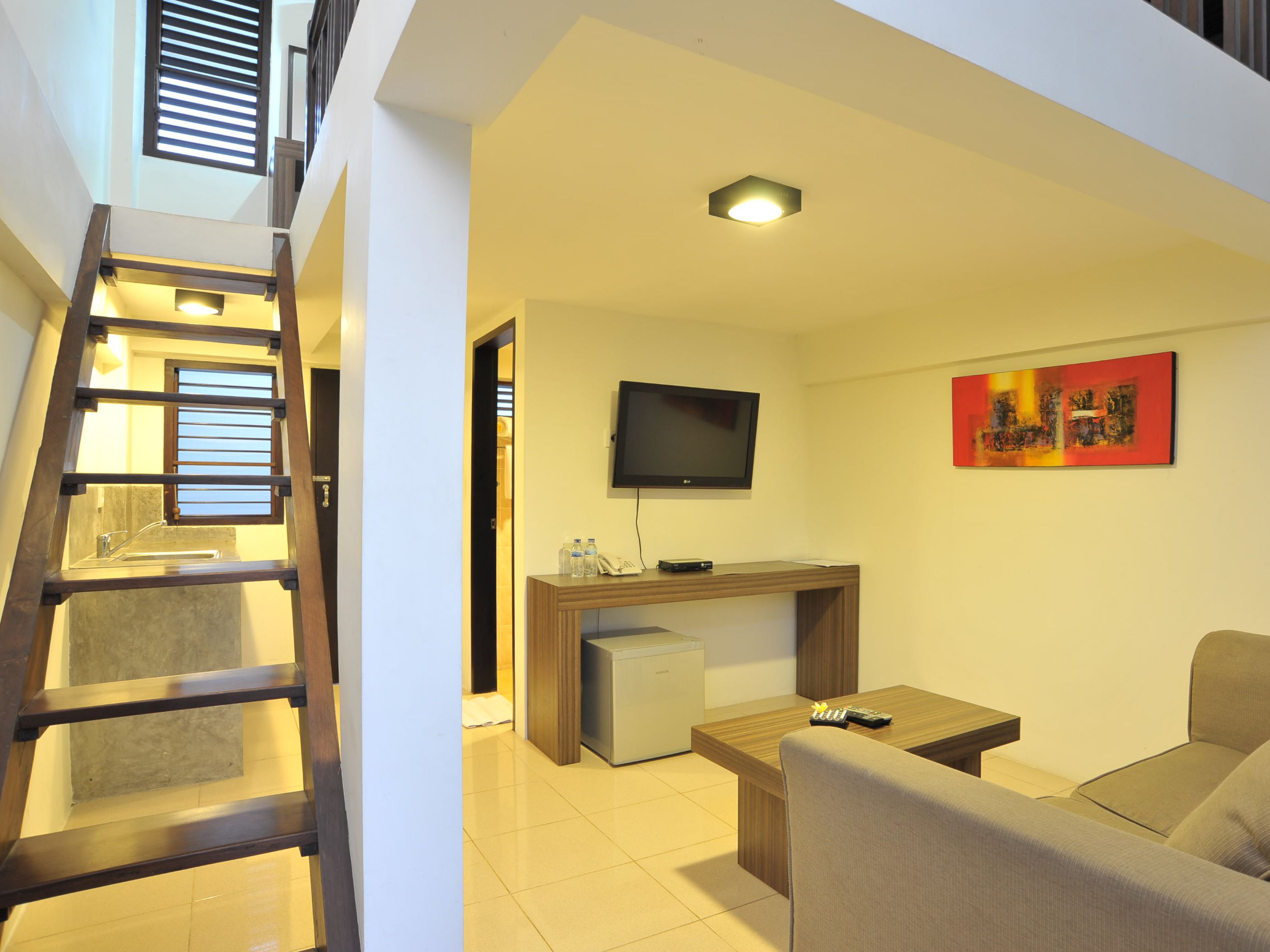 A modern living room with a sofa, a coffee table, a TV, and a desk. There is a staircase with a railing leading to an upper level.