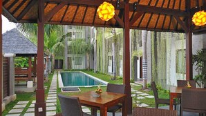 A covered outdoor area with a pool, wooden furniture, and a thatched roof. - Ganga Hotel & Apartments (Denpasar)
