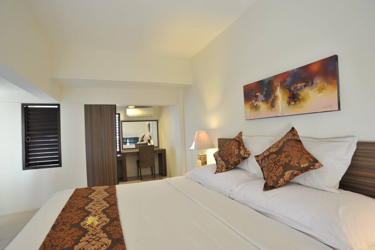 A hotel room with a bed, a desk, a chair, and a painting on the wall.