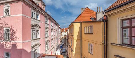 Une rue étroite bordée de bâtiments aux couleurs vives, dotés d’une architecture traditionnelle, notamment un bâtiment rose aux encadrements de fenêtres richement décorés et un bâtiment jaune surmonté d’un toit recouvert de tuiles rouges.