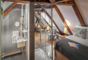 A modern loft bedroom with a glass shower, wooden beams, a bed with a magazine, and a small table with a lamp. - 3 Epoques Apartments by Adrez Living (Prague)