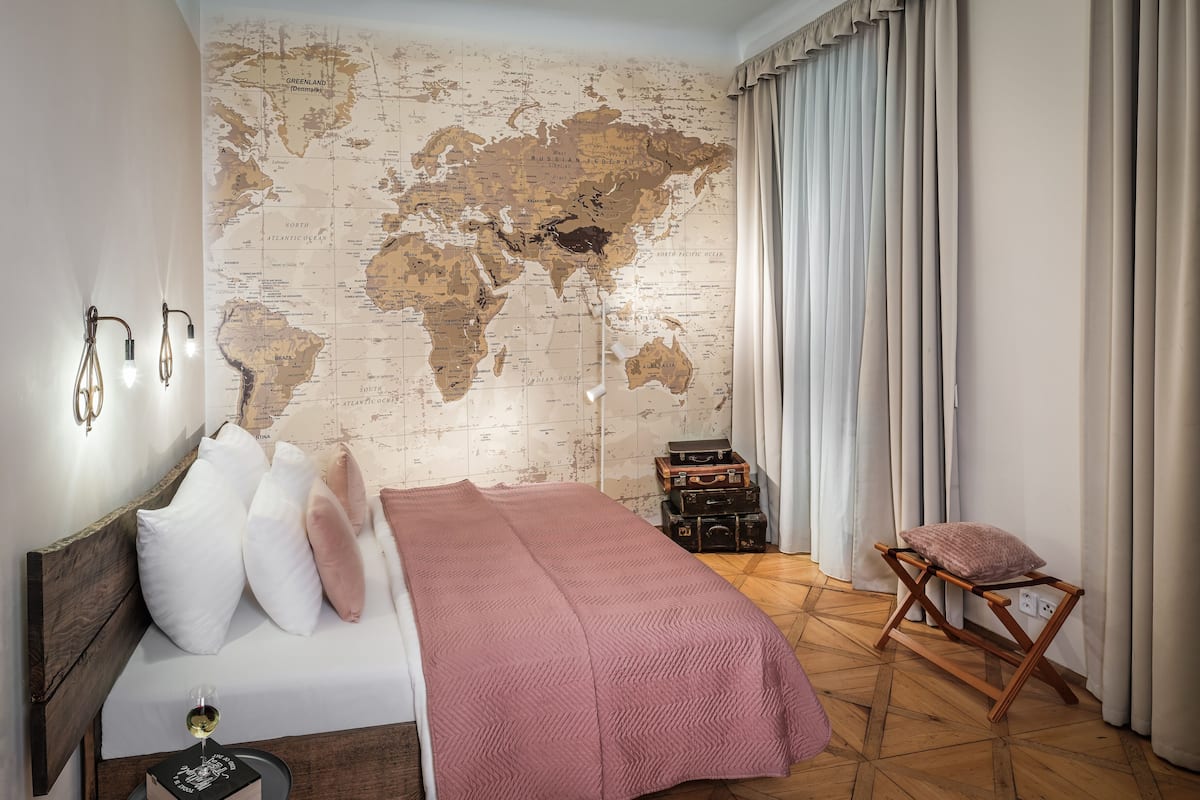 Ein Schlafzimmer mit einer Weltkarte an der Wand, einem Bett mit Kissen, einem Holz-Nachttisch und einem kleinen Tisch mit einem Glas Wein.